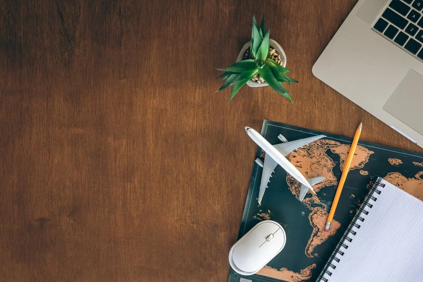 Miniaturflugzeug, Notizblock, Weltkarte und Laptop auf einem Holztisch.